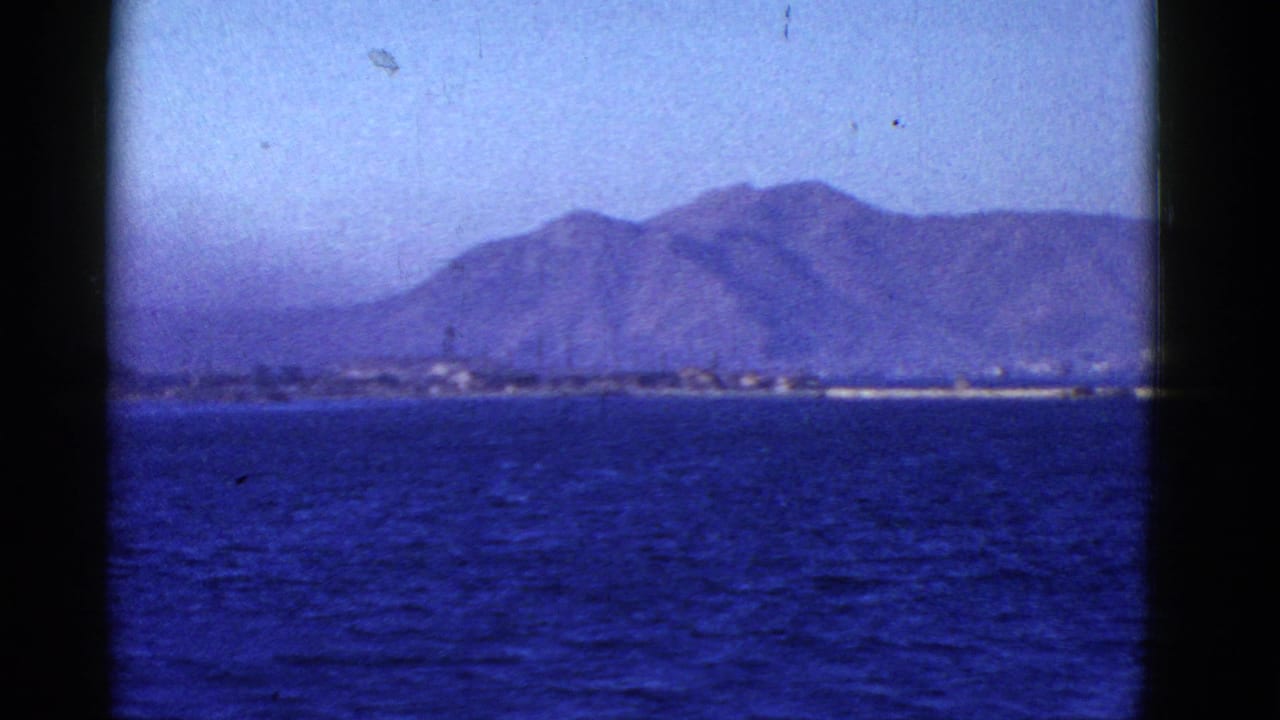 Distant mountains and shoreline across blue water under a hazy sky.