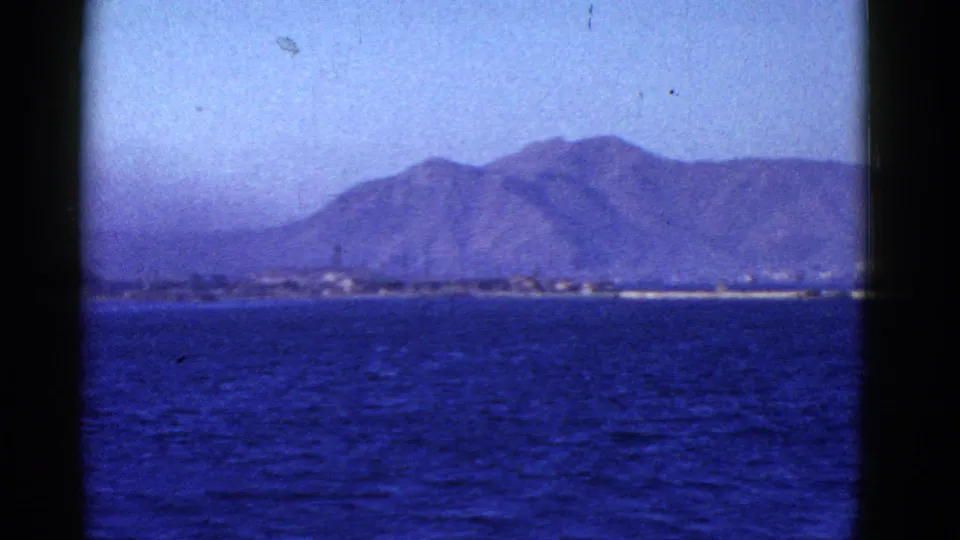 Archival 8mm frame of blue water and a distant mountain shoreline, likely filmed from a vessel near San Francisco.