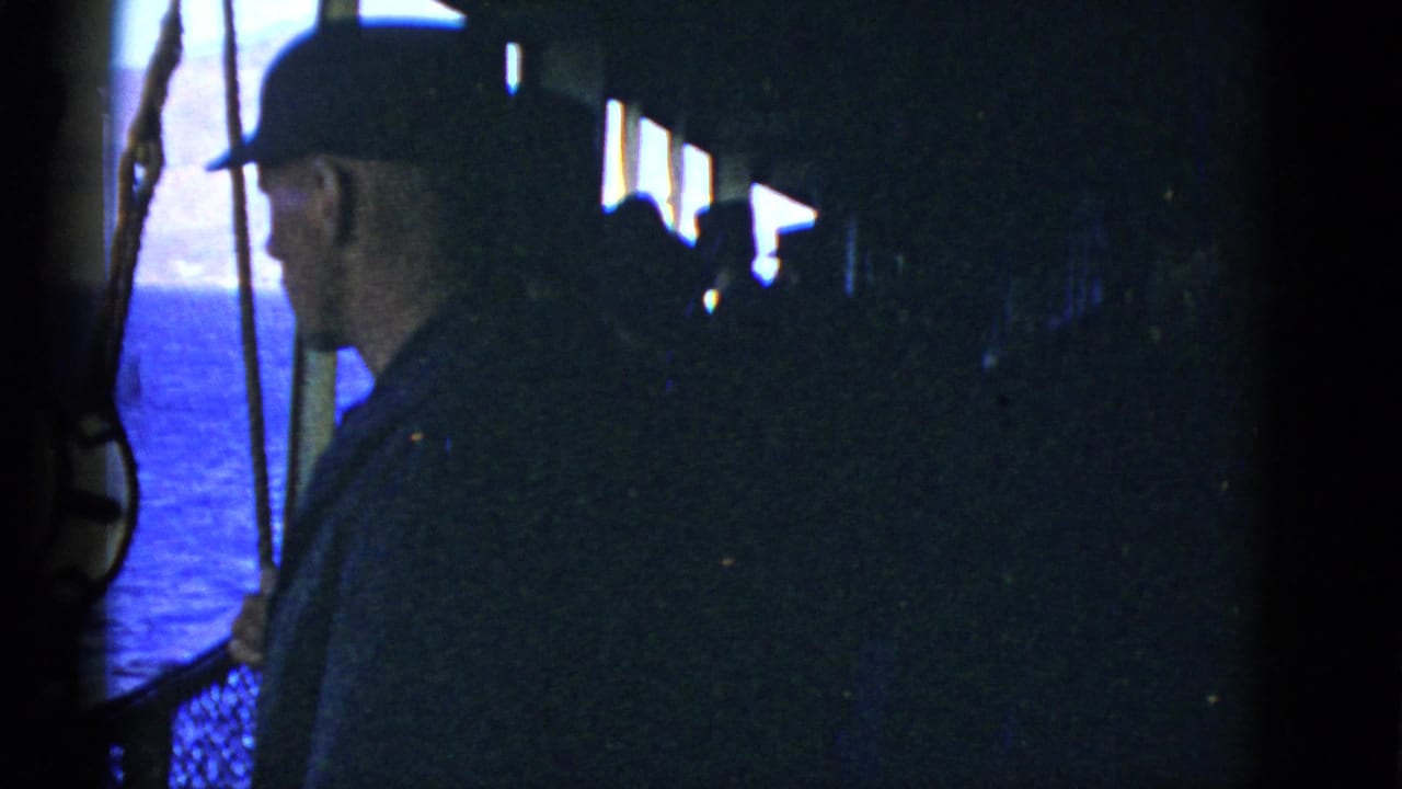 1950s 8mm frame of a man in a dark cap on a ship deck, seen in profile against the ocean near San Francisco.