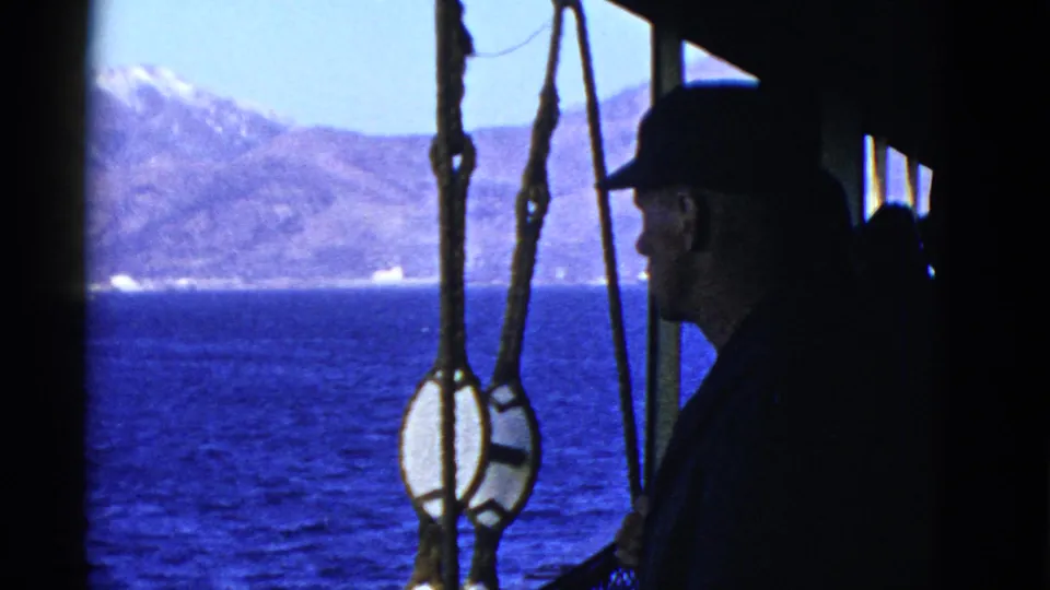 In 1952 San Francisco-area home-movie footage, a man in a dark cap stands in silhouette beside rigging with water and mountains beyond.