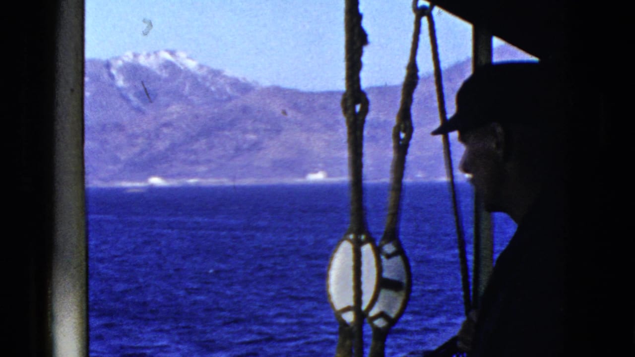 Boat rigging frames blue water, mountains, and a silhouetted man at right.