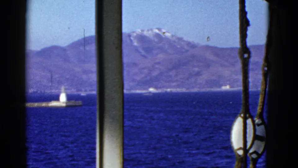 The final frame holds on water, distant mountains, a small lighthouse or beacon, and rigging beside a silhouetted passenger.
