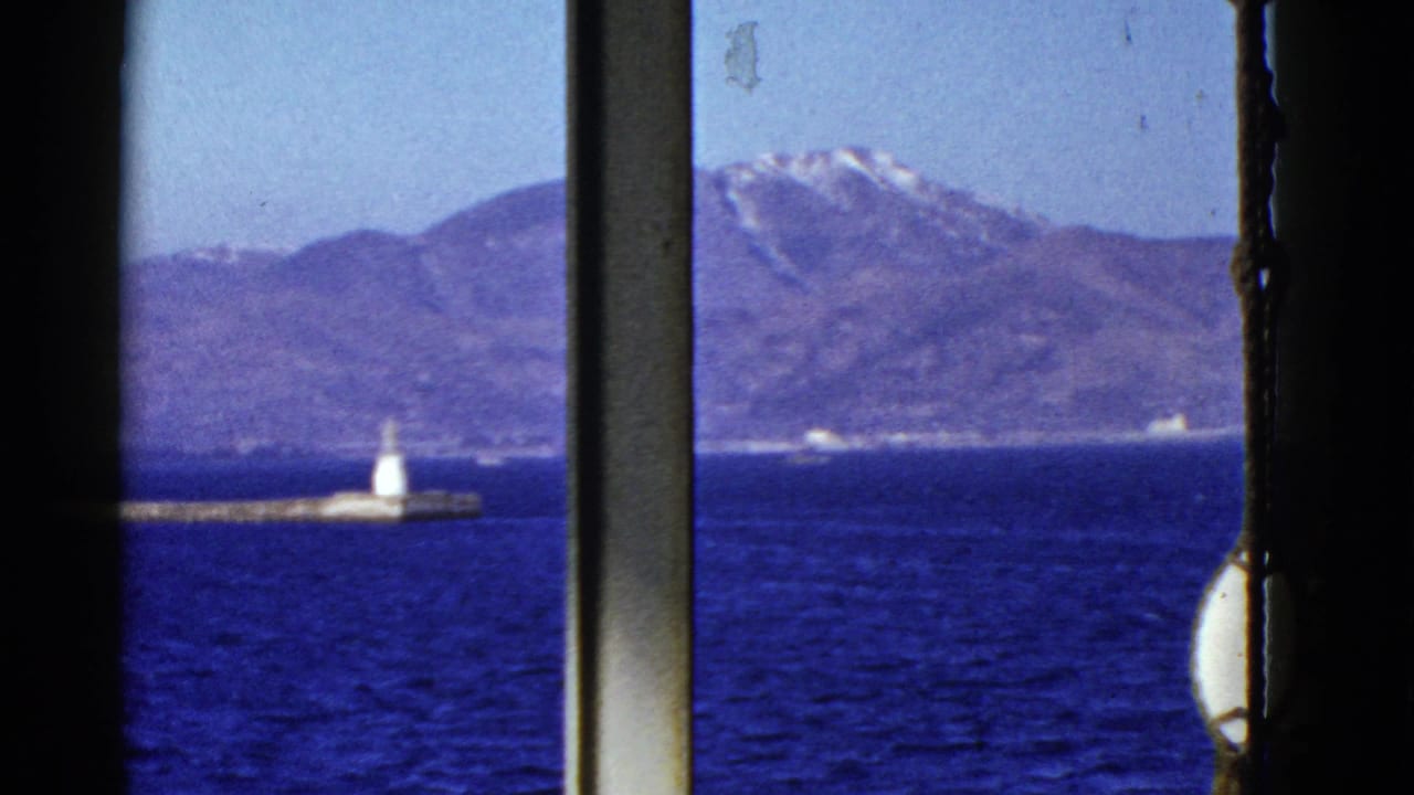 Early 1950s San Francisco Bay view through a vessel window, showing blue water, a low pier, a white beacon, and distant mountains.