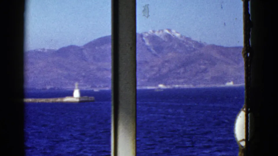 Early 1950s San Francisco Bay view through a vessel window, showing blue water, a low pier, a white beacon, and distant mountains.