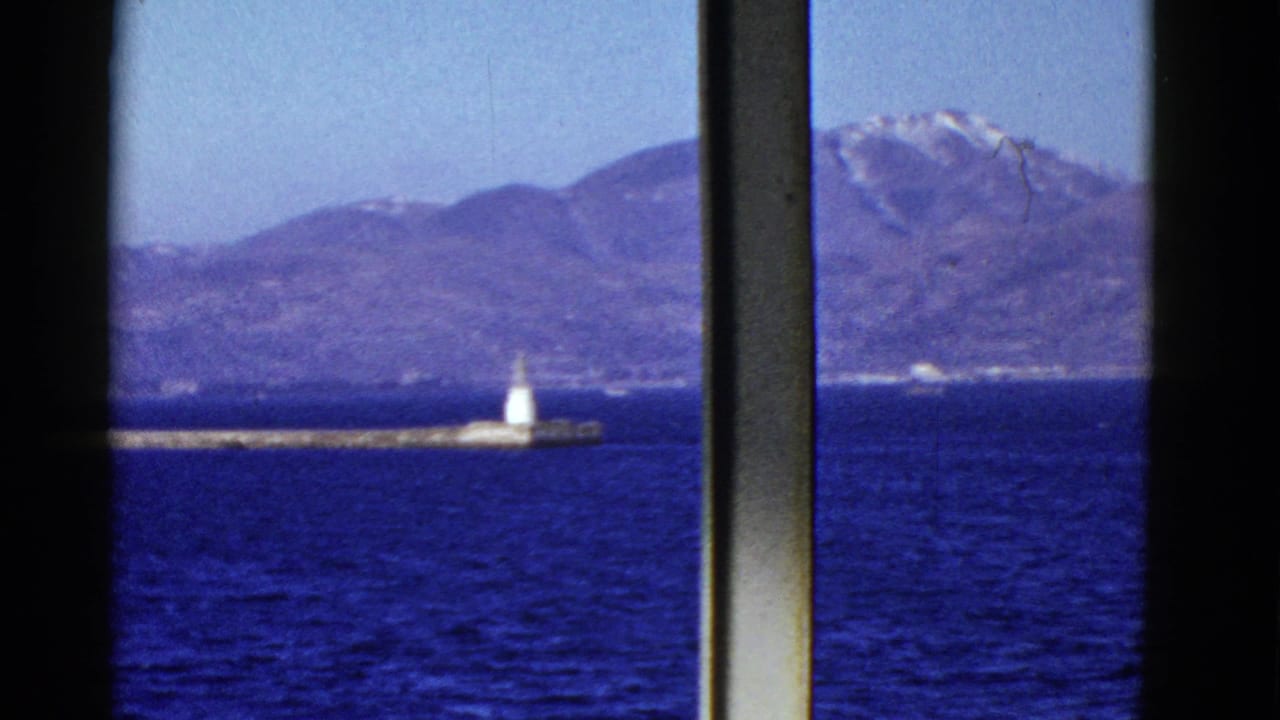 Distant mountain shoreline and white pier beacon viewed past vertical ship window bars.