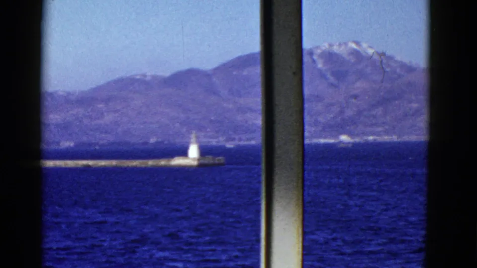 Early 1950s San Francisco Bay footage shows a distant white beacon on a pier, dark blue water, and mountains through ship window framing.