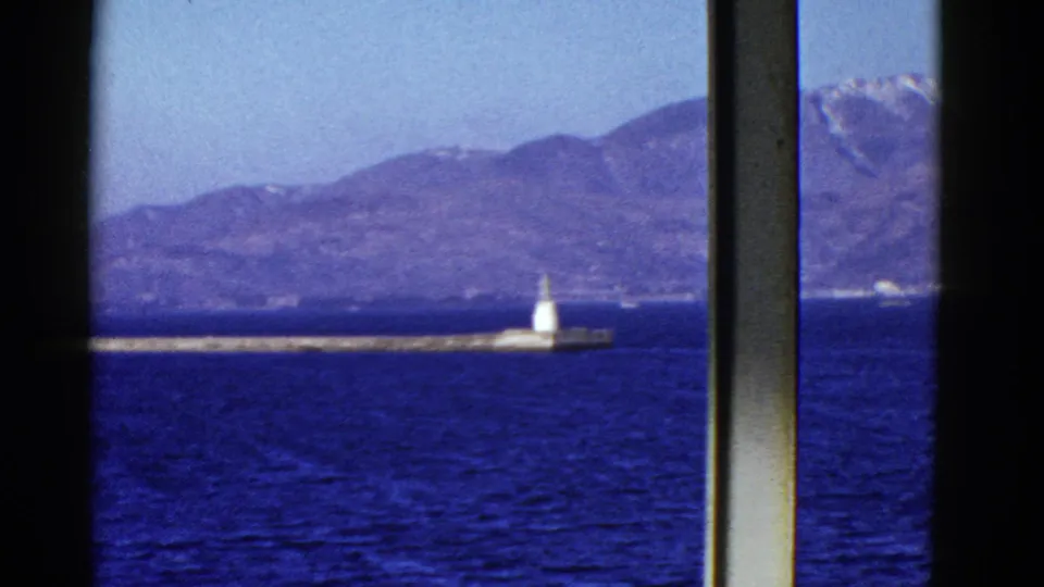 Early 1950s San Francisco Bay view centers on a white beacon along a low pier, with rippled blue water and hazy mountains beyond.
