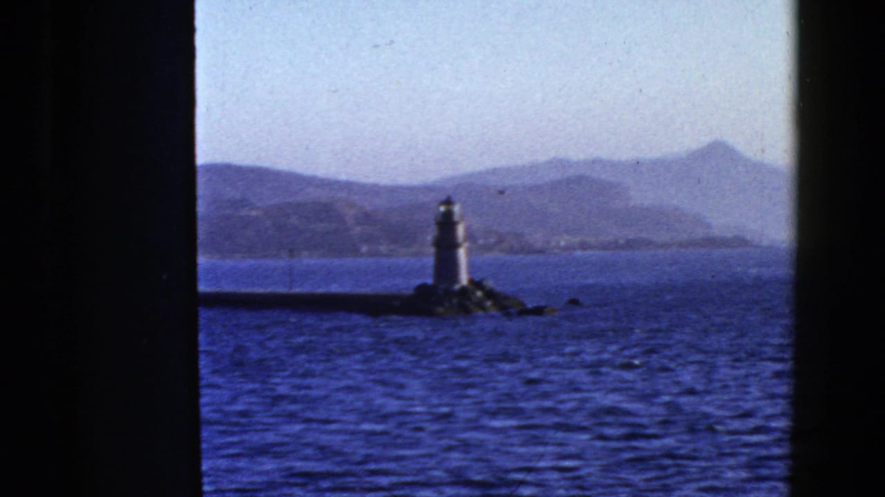 Lighthouse centered beyond dark window framing with bay water and hills in the background.