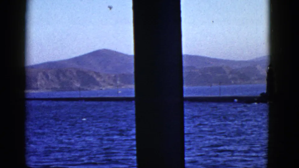 1950s San Francisco Bay frame with dark vertical bars, blue water, distant hills, and the lighthouse partly cropped at the right edge.