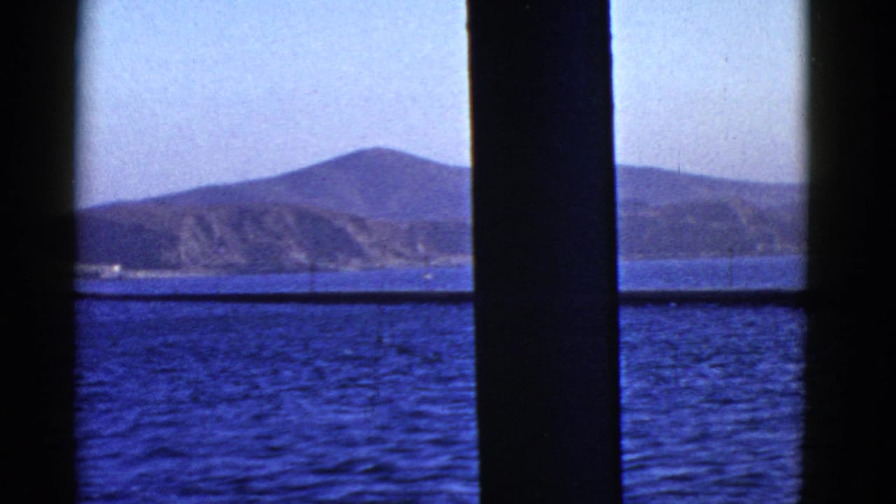1950s San Francisco-area 8mm view of blue bay water and distant hills framed by dark window or railing bars.
