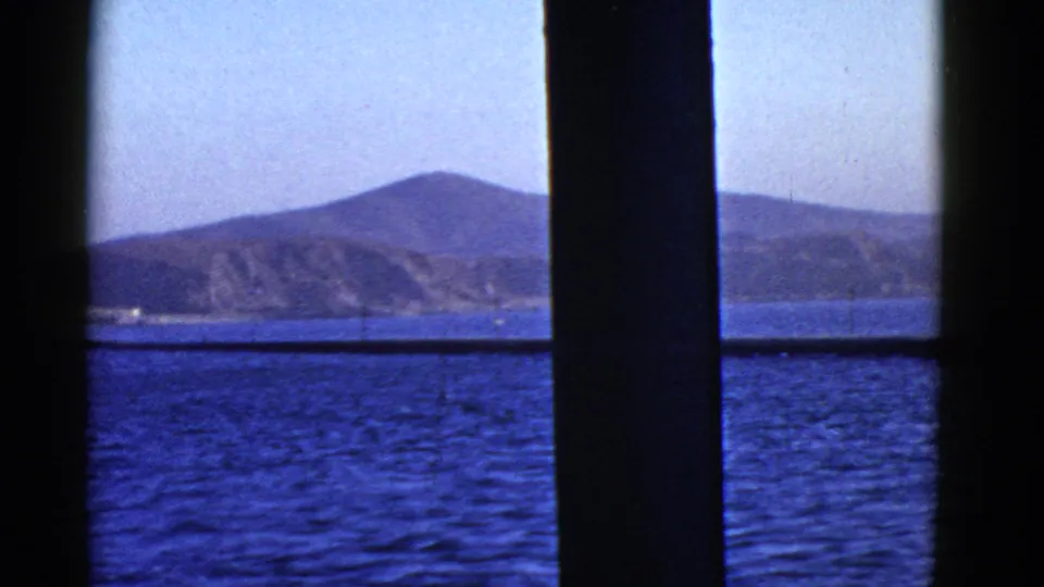 1950s San Francisco-area 8mm view of blue bay water and distant hills framed by dark window or railing bars.