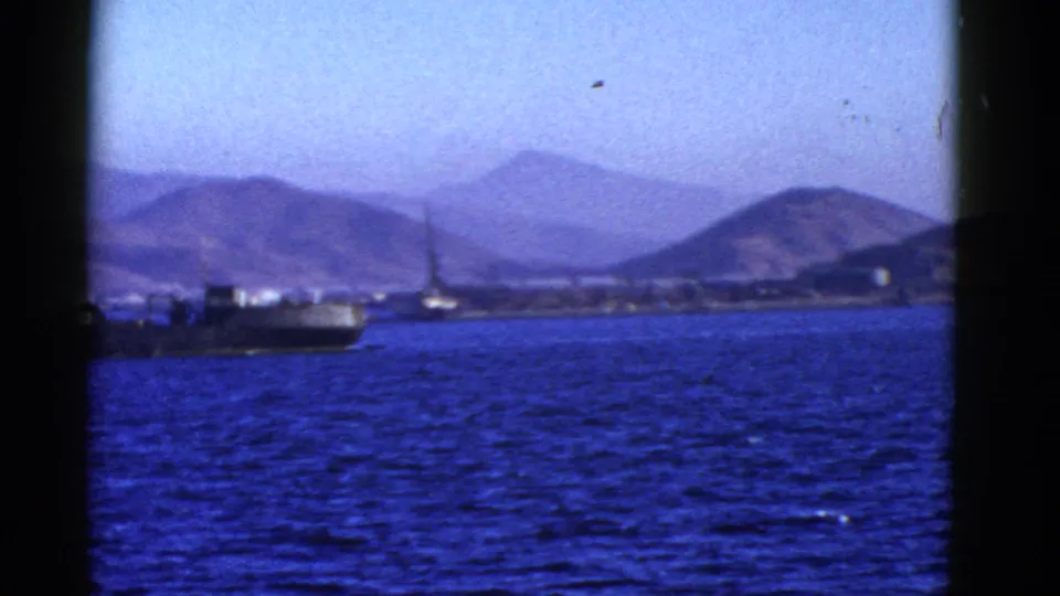 1952 San Francisco harbor view with a large ship moving across blue water before distant hills and low waterfront structures.