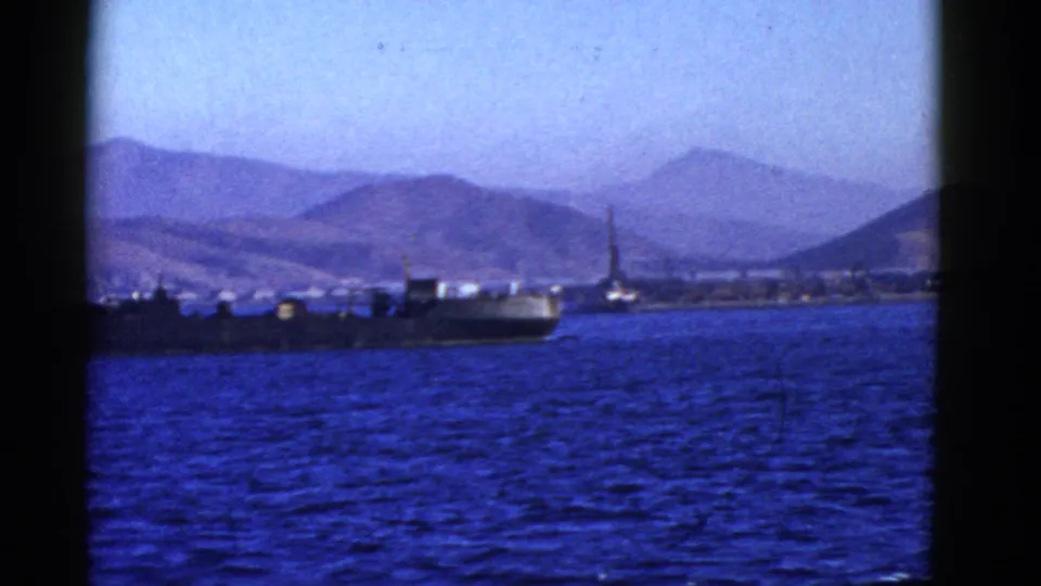 1952 San Francisco harbor frame showing a large ship near the foreground, blue water, distant hilly shoreline, and a crane or mast beyond.