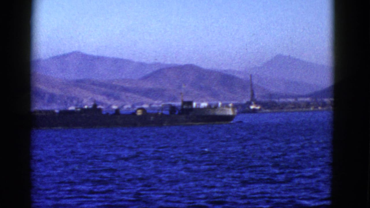 A large dark cargo ship moves across blue water near a mountainous shoreline, consistent with the supplied 1952 San Francisco-area metadata.