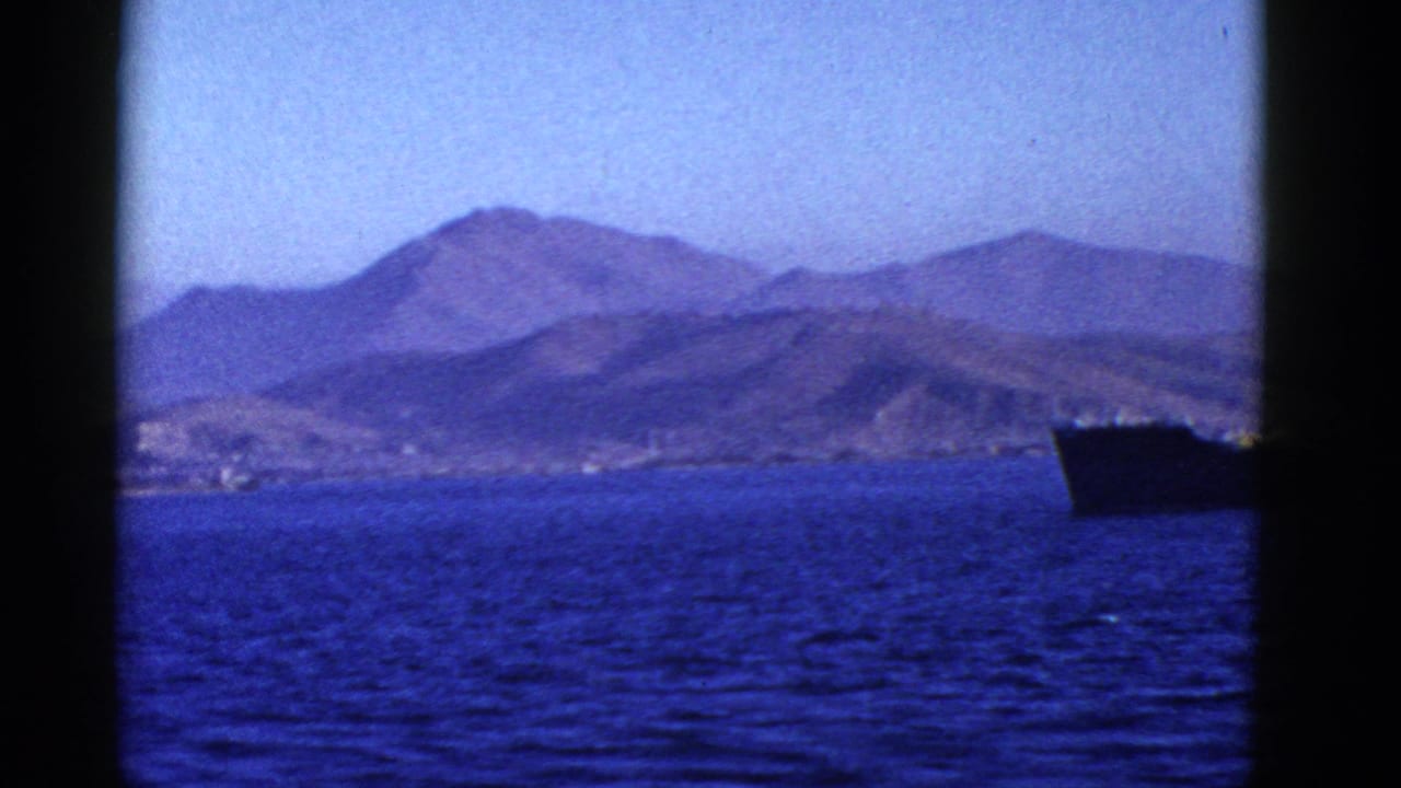 1950s San Francisco-area boat view of blue water, distant rugged hills, and a large dark ship near the horizon.