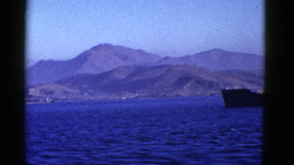 1950s San Francisco-area boat view of blue water, distant rugged hills, and a large dark ship near the horizon.