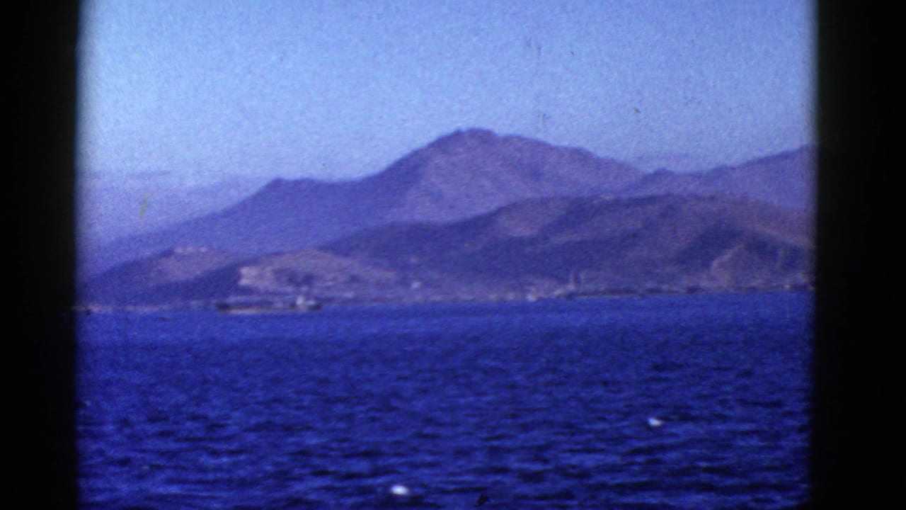 Distant mountain ridge and shoreline seen across blue water.