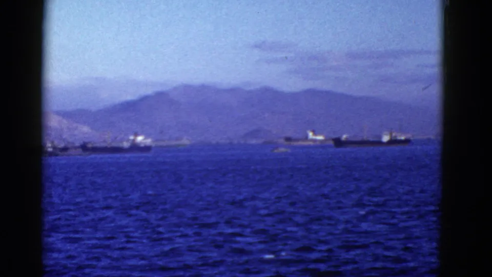 Early 1950s San Francisco Bay home-movie frame showing a cargo ship, another vessel near shore, blue water, and hazy hills.