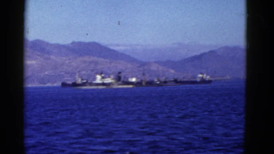 A mid-century 8mm view of a long ship on San Francisco Bay, with mountains and blue water in the background.