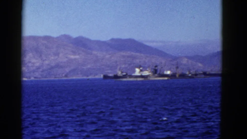 Early 1950s San Francisco Bay scene with a large ship near shore, blue water, and hazy mountains beyond.