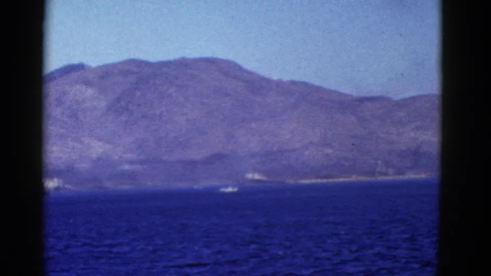Home-movie frame of bay water and a distant hilly island or shoreline, filmed from a moving boat in the San Francisco area.