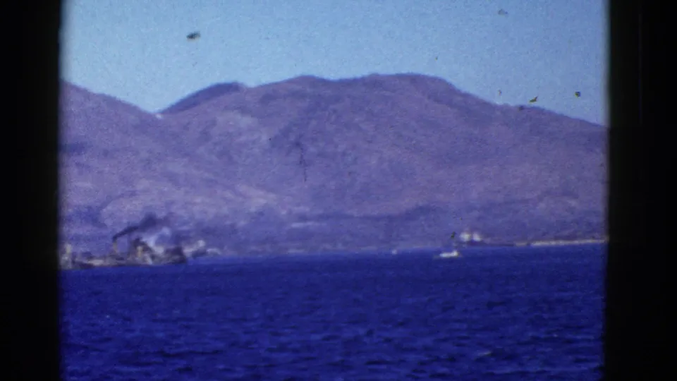 San Francisco Bay home-movie view showing blue water, a small boat, distant hills, and dark film or window framing.