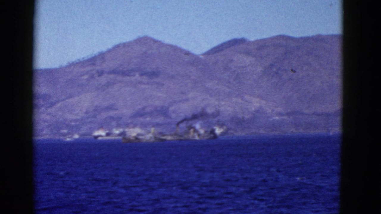 Distant shoreline and mountains across blue water, with smoke or haze near waterfront structures.