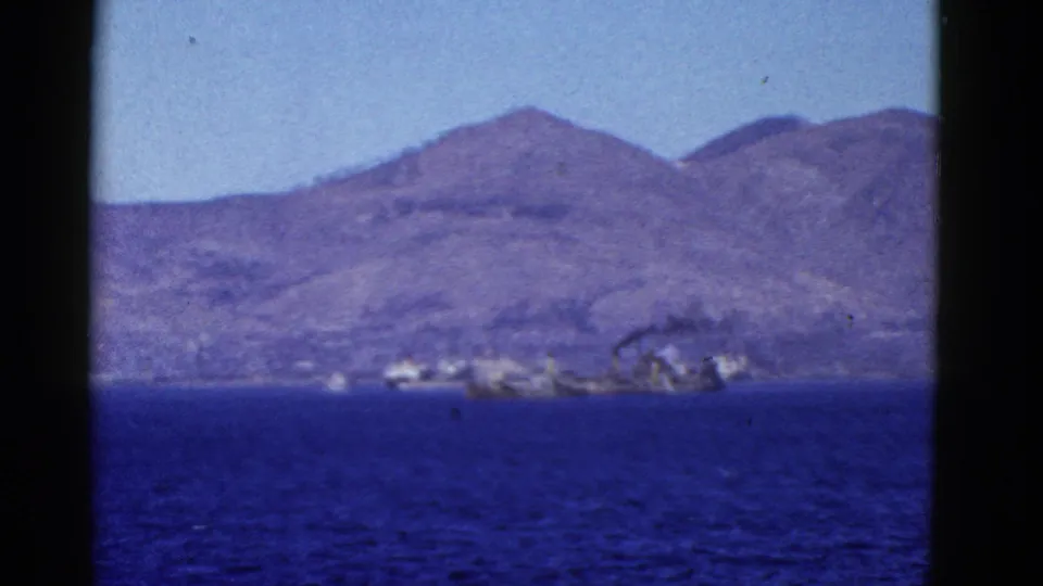 1950s 8mm frame of San Francisco-area water, distant mountains, and a small bright vessel or structure along the shoreline.