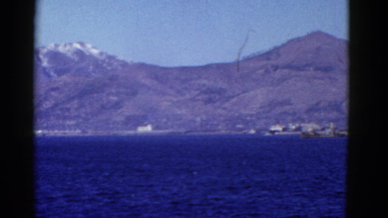 Distant coastal mountains and shoreline structures viewed across blue water.