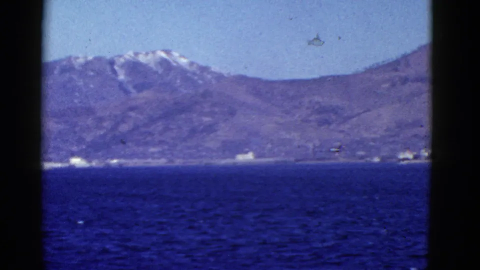 1952 8mm coastal view near San Francisco, showing dark blue water, a hazy mountain ridge, and small pale structures along the shore.