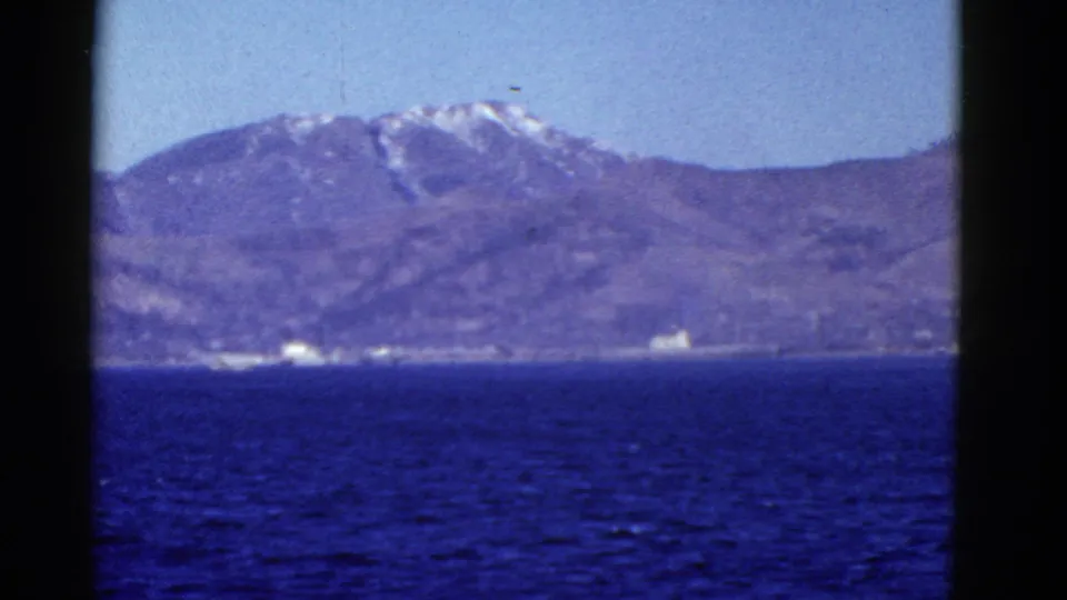 1952 San Francisco-area home-movie frame with bay water in front, hazy mountains beyond, and small structures along the distant coast.