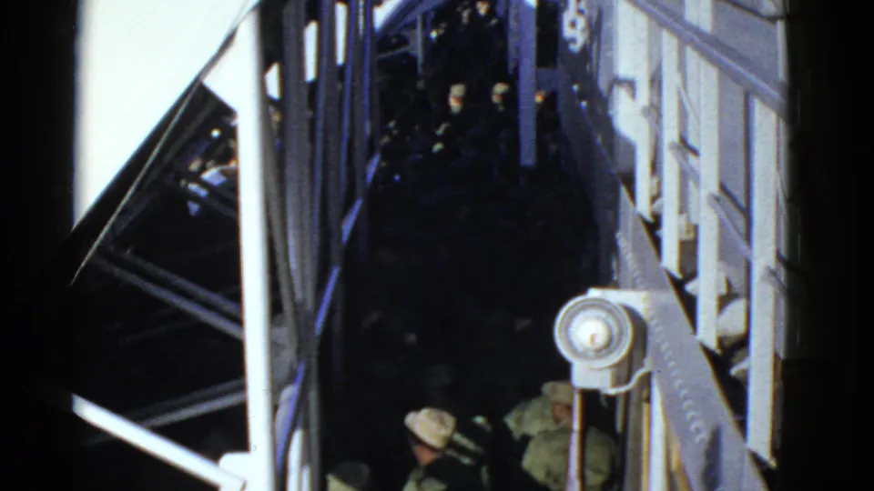 Early 1950s San Francisco home-movie frame with uniformed men moving below white railings and metal supports at night.