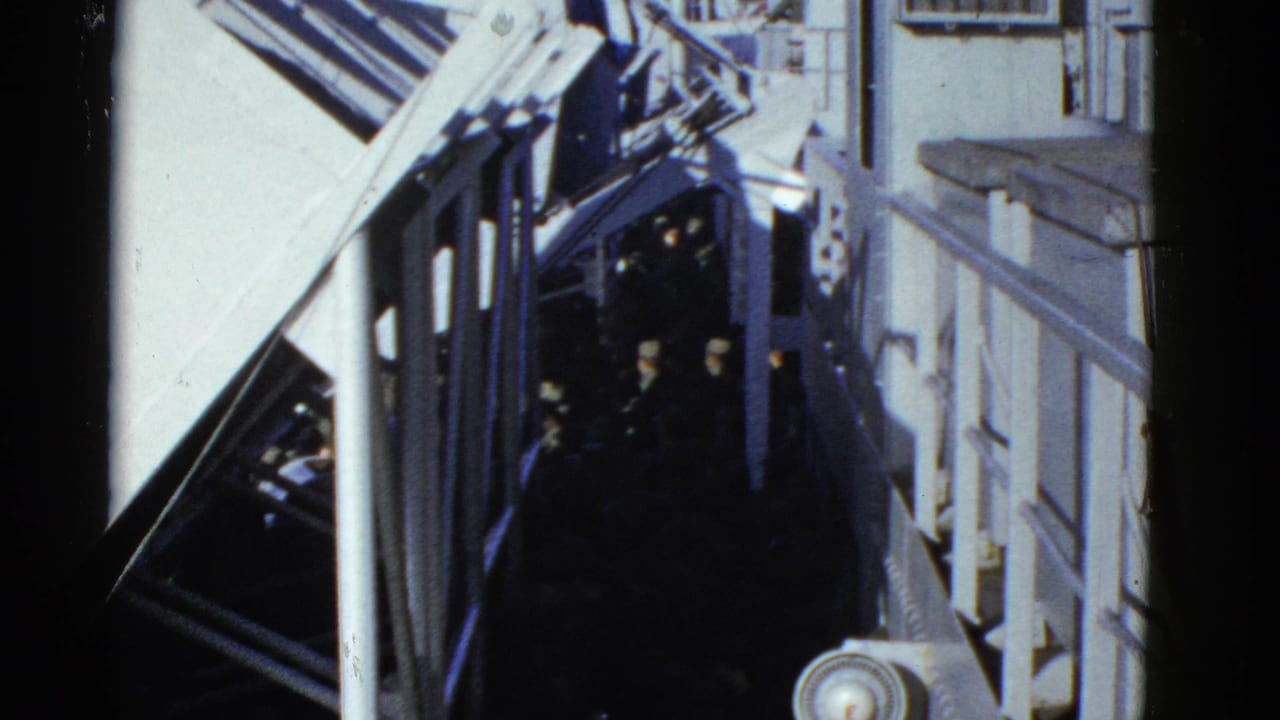 1952 San Francisco home-movie frame showing dark-uniformed people moving through a narrow ship passage with white railings and beams.