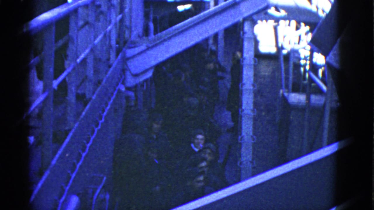 1950s San Francisco waterfront home-movie frame showing elevated dock walkways, railings and several people in low light.