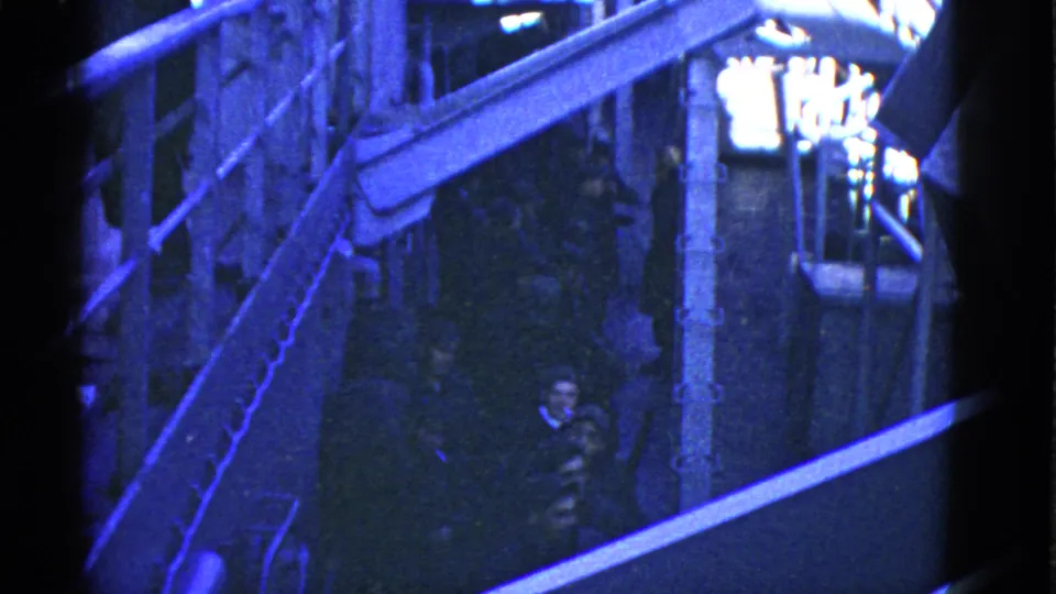 1950s San Francisco waterfront home-movie frame showing elevated dock walkways, railings and several people in low light.