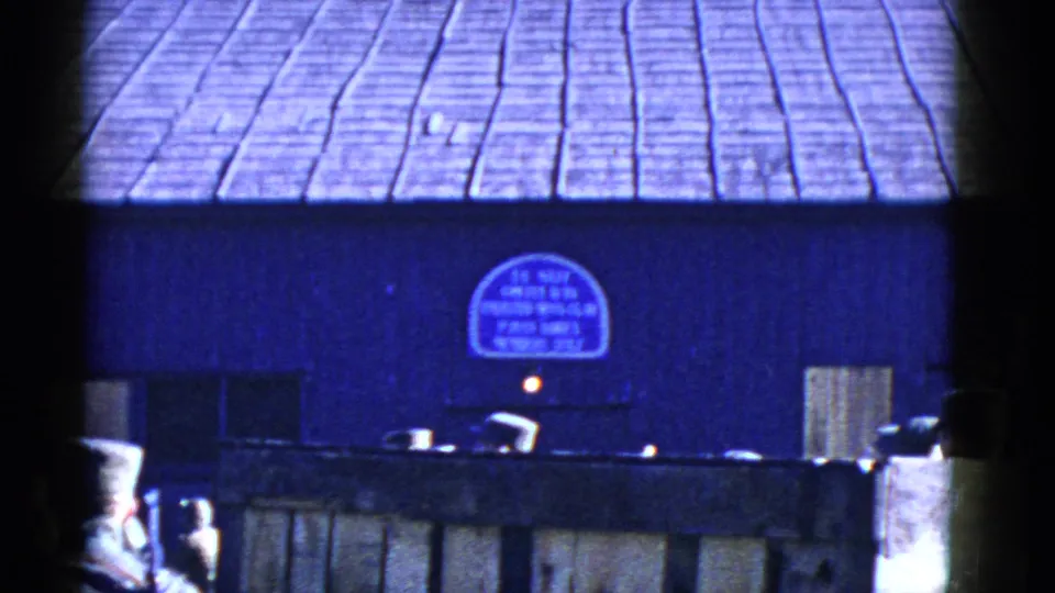 1950s San Francisco waterfront frame showing a shingled roof, small sign and dark dockside foreground with vehicles or equipment below.