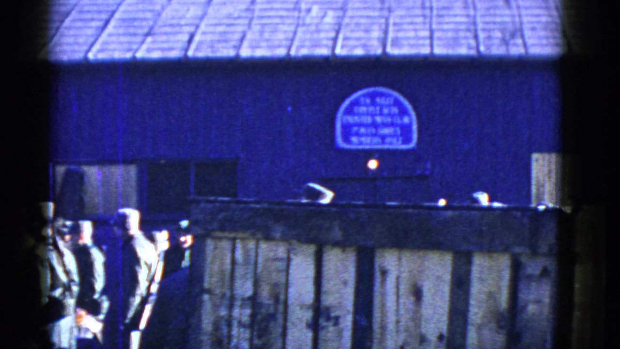 Uniformed men, some carrying rifles, gather near a wooden fence outside a blue building in the San Francisco home-movie footage.