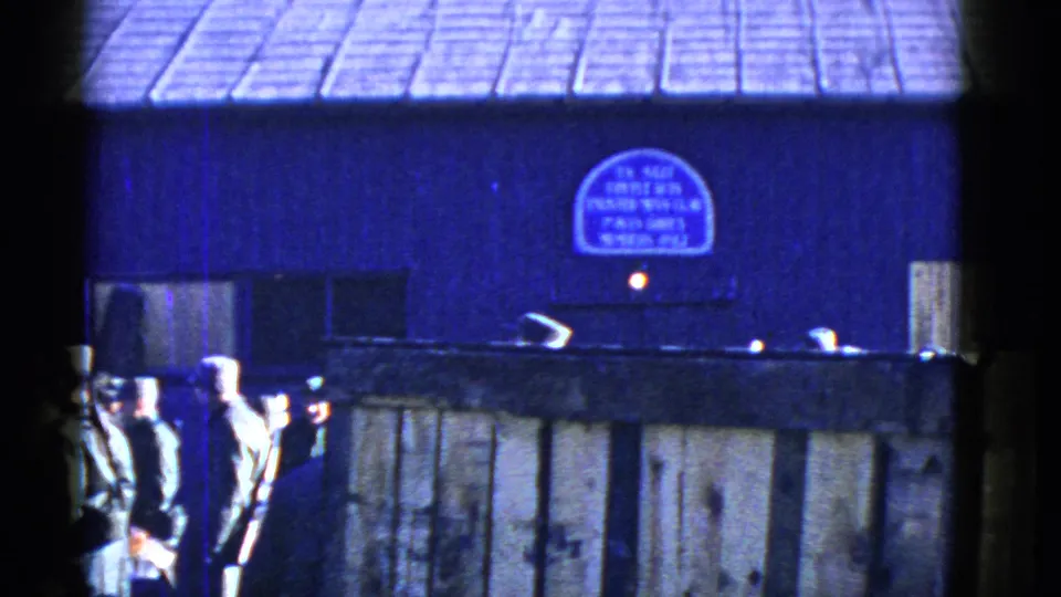 Uniformed men, some carrying rifles, gather near a wooden fence outside a blue building in the San Francisco home-movie footage.