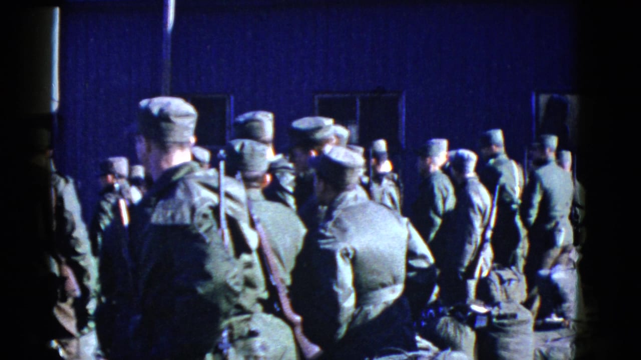 A dense group of soldiers in uniform stands near windows on a dark exterior wall.
