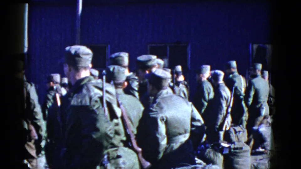 1952 San Francisco frame with uniformed soldiers, rifles, packs, and caps gathered beside a dark blue building.