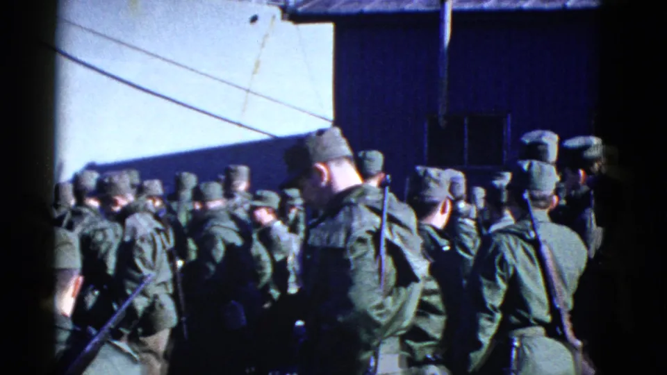 1952 San Francisco 8mm frame showing soldiers with rifles and field gear assembled near a dark exterior wall.