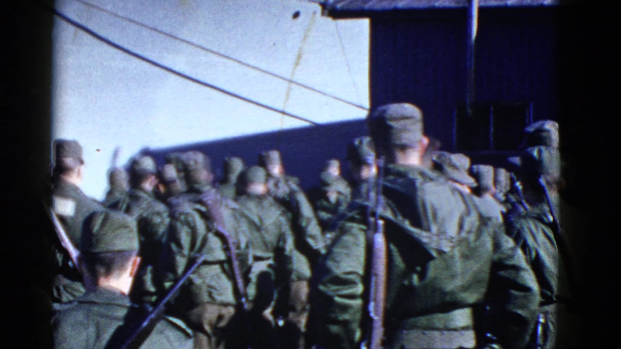 1950s San Francisco home-movie frame showing uniformed troops with rifles assembled near a ship hull in bright daylight.