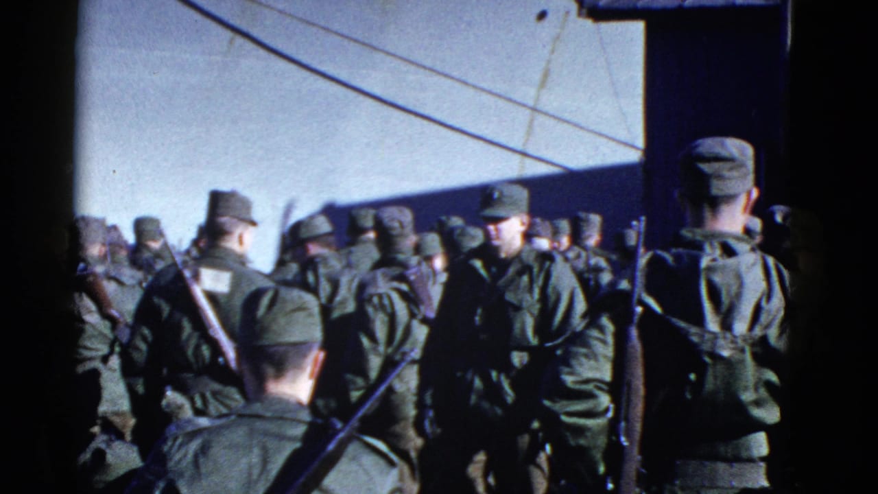 Uniformed troops, some with rifles slung over their shoulders, assemble beside a large ship in archival 8mm footage.