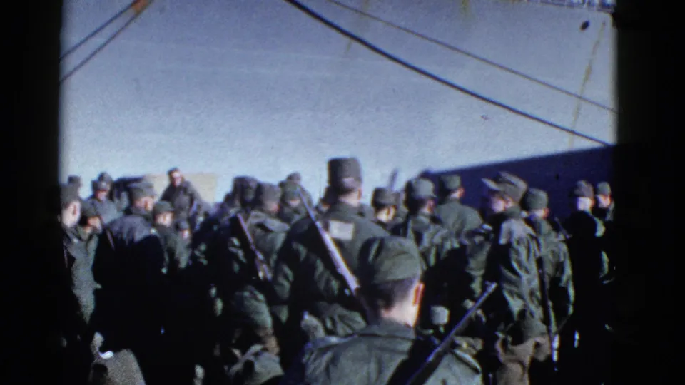 Wide 8mm view of uniformed troops assembled near a ship, with rifles, caps, rigging lines, and bright sky visible.