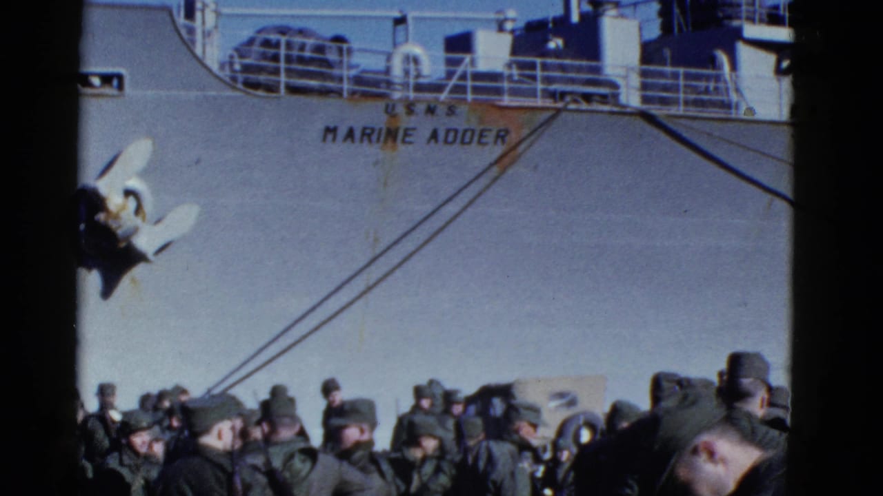 Uniformed men stand below the hull of the U.S.N.S. Marine Adder with anchor and rigging visible.