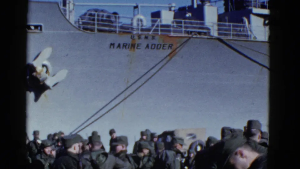 1952 San Francisco pier footage showing uniformed men beneath the U.S.N.S. Marine Adder hull, with anchor, railings, and mooring lines visible.