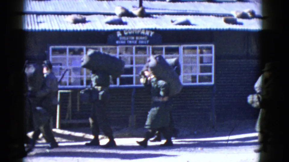 Military personnel continue walking past the A Company building, carrying bags and packs in a San Francisco waterfront setting.