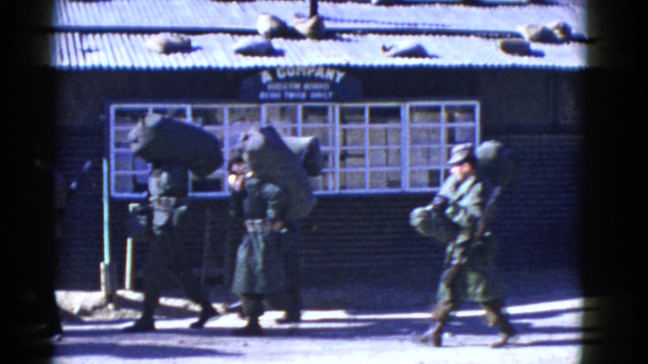 In supported San Francisco 1950s home-movie footage, uniformed soldiers with rifles and packs pass a windowed barracks-like building marked A Company.
