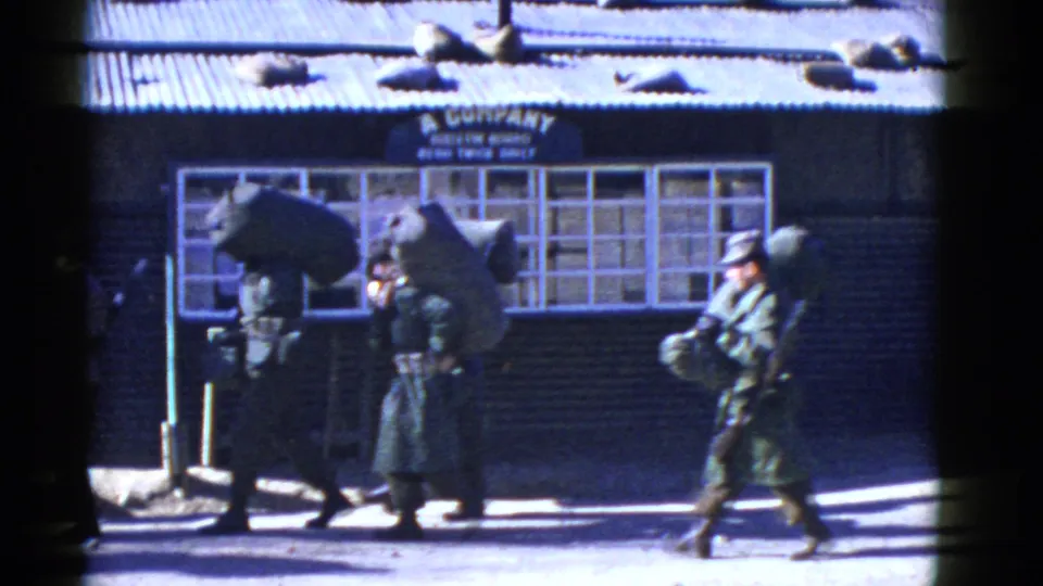 In supported San Francisco 1950s home-movie footage, uniformed soldiers with rifles and packs pass a windowed barracks-like building marked A Company.