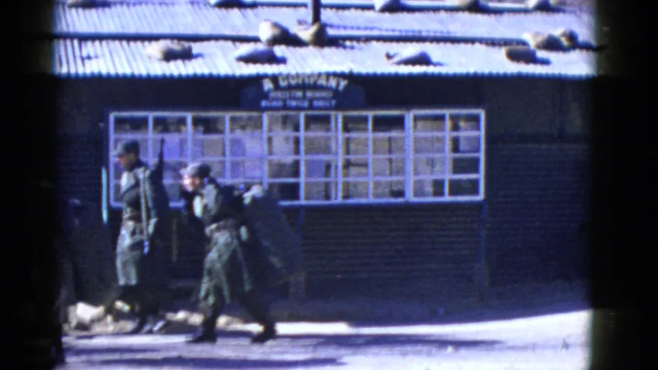 Near the end of the clip, two uniformed soldiers carrying rifles and packs pass below the A Company sign and multi-pane windows.